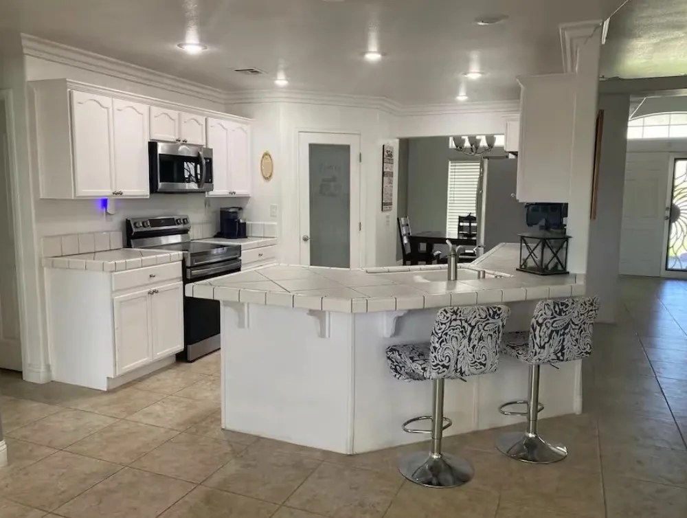 The kitchen at Peaceful Mountain Views, with white cabinets, a tiled counter and two bar stools
